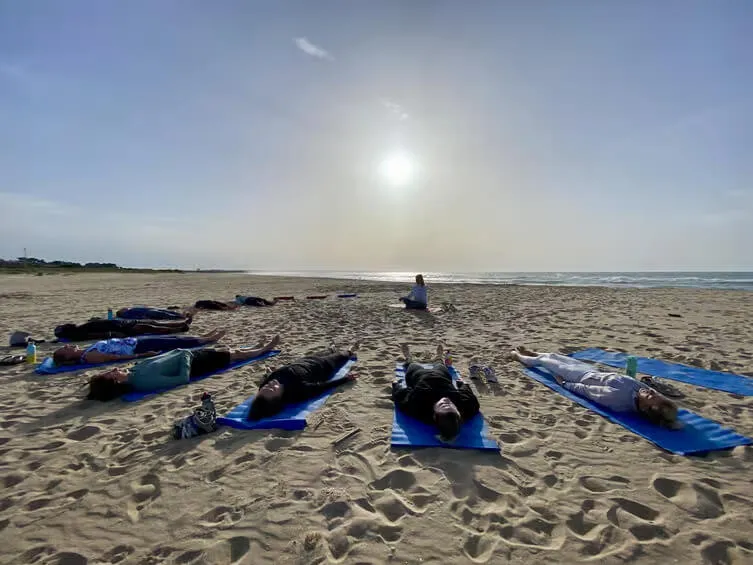 Group practicing Hatha sunset yoga in Portimão on a sandy beach surrounded by ocean cliffs.