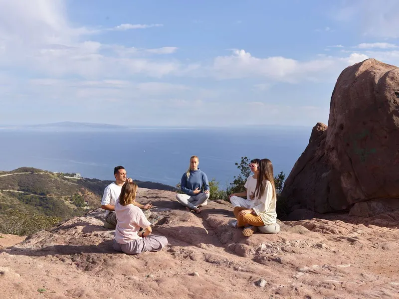 A group of peaceful hikers sitting in meditation on a lush green volcanic trail on Pico Island, overlooking the Atlantic Ocean.