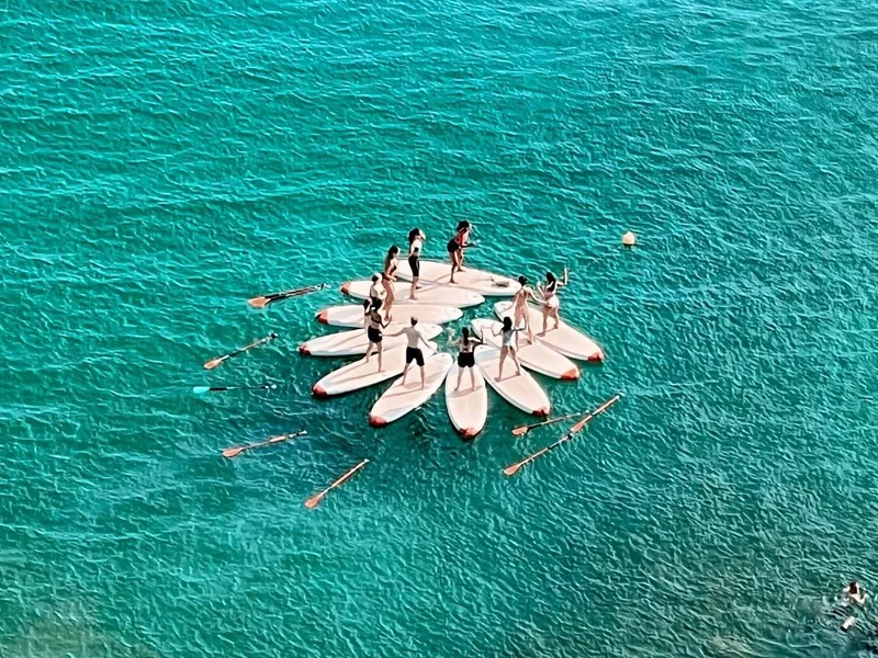 Um grupo de participantes a praticarem Yoga numa prancha de stand-up paddleboard nas águas calmas do oceano com os cenários dos Penhascos da Falésia ao fundo.