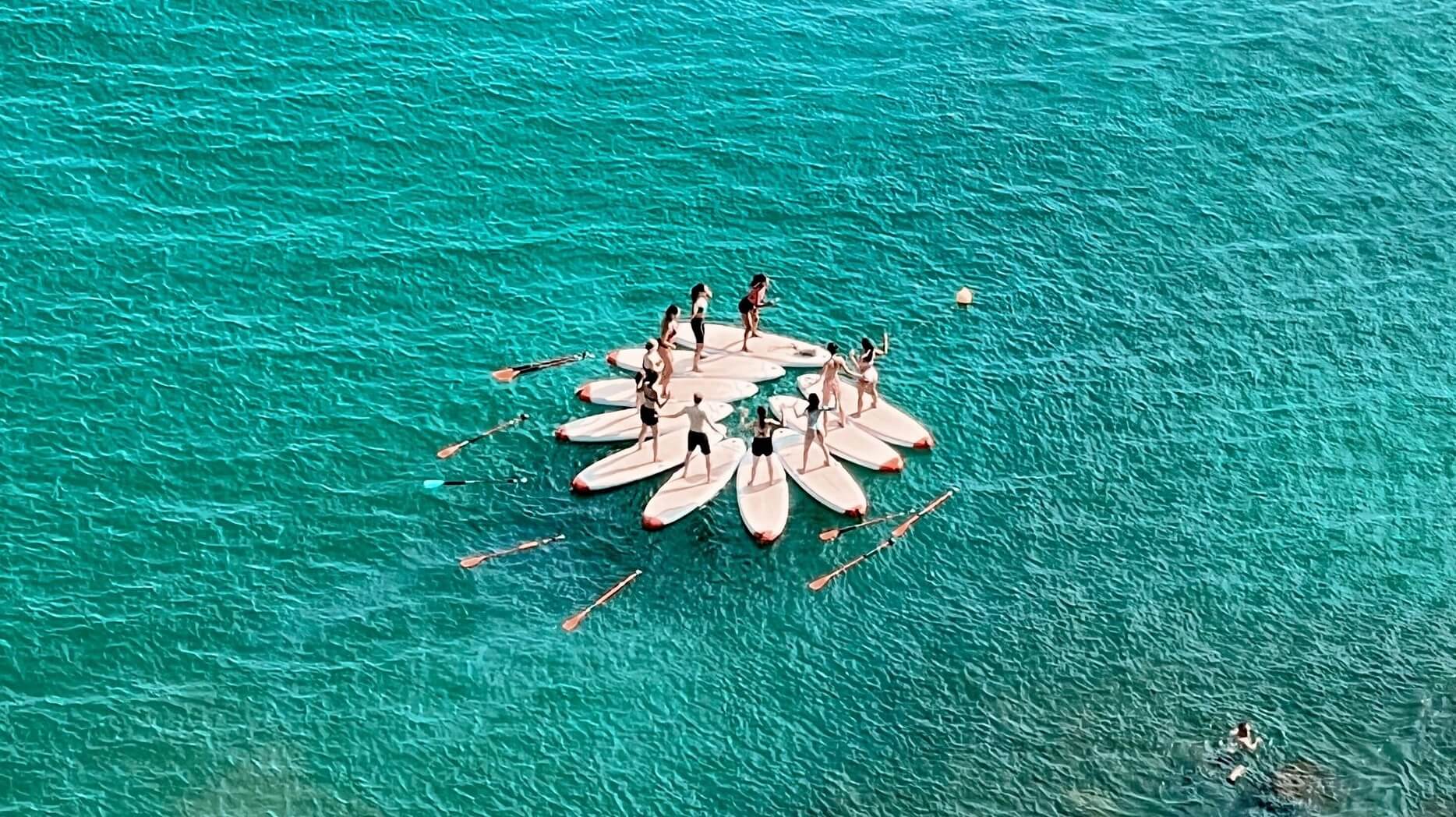 A group of participants practicing yoga on a stand-up paddleboard on the calm ocean waters with the scenic Falésia Cliffs in the background.