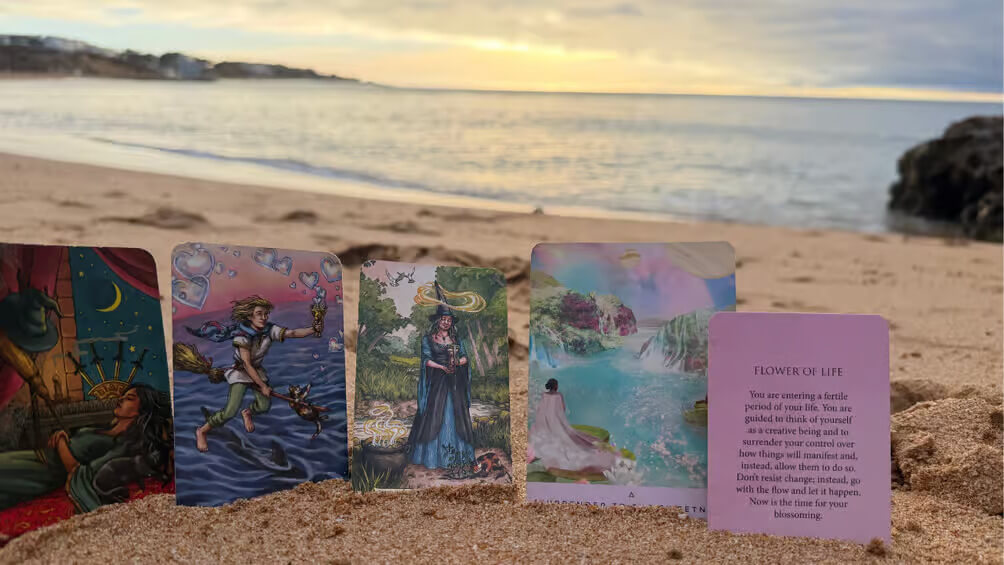 Uma configuração calma e acolhedora para uma leitura espiritual numa bela praia arenosa de Albufeira, com cartas de tarot e oráculo perto das ondas suaves do oceano.