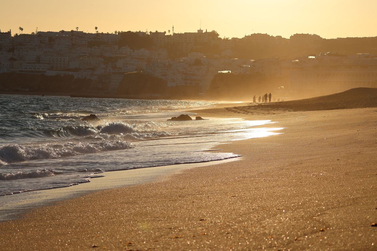 Participante a praticar Breathwork ao pôr do sol em Albufeira enquanto está sentado na areia da praia virado para o oceano.